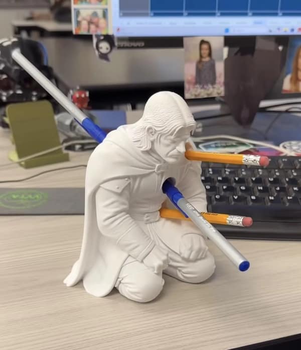 dark but funny lord of the rings meme showcasing a desk pen holder shaped like the kneeling, dying Boromir, with several pens and pencils sticking through his chest where the Uruk-hai arrows originally hit.
