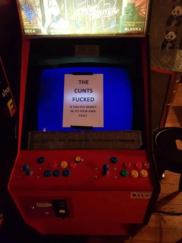 hilarious meme showing a broken Street Fighter cabinet featuring a brutally honest paper sign warning players that the machine is completely broken and losing money in it is their own fault.