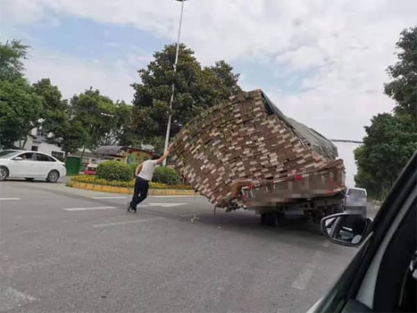 A man desperately leaning against a massive, tipping load of lumber on a truck.