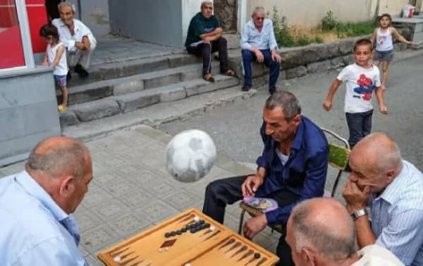 A soccer ball frozen in mid-air inches away from ruining an outdoor backgammon game.