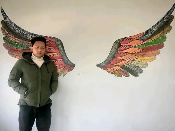 Man standing against a white wall with colorful angel wings painted behind him for a photo.