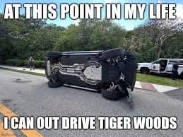 A punny Tiger Woods crash meme showing his wrecked SUV on its side with the bold text: "At this point in my life I can out drive Tiger Woods," mocking his literal driving skills compared to his legendary status with a golf driver.