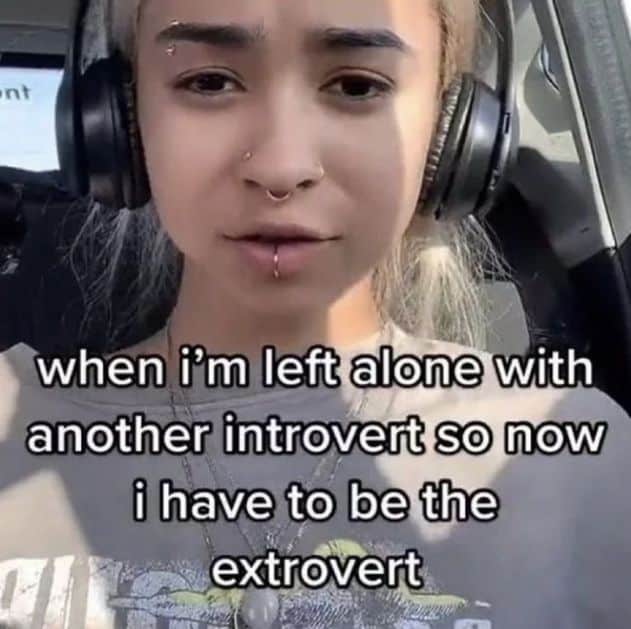 A front-facing camera unhinged screenshot of a girl with facial piercings and headphones. The text explains a common social nightmare for the quiet ones: "when i’m left alone with another introvert so now i have to be the extrovert."