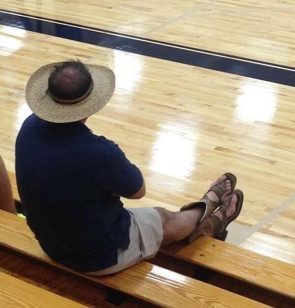 masterclass in questionable choices featuring a man in a "sun-roof" straw hat that leaves his balding crown exposed, paired with "cowboy boots" that have been surgically altered into thong-style sandals.