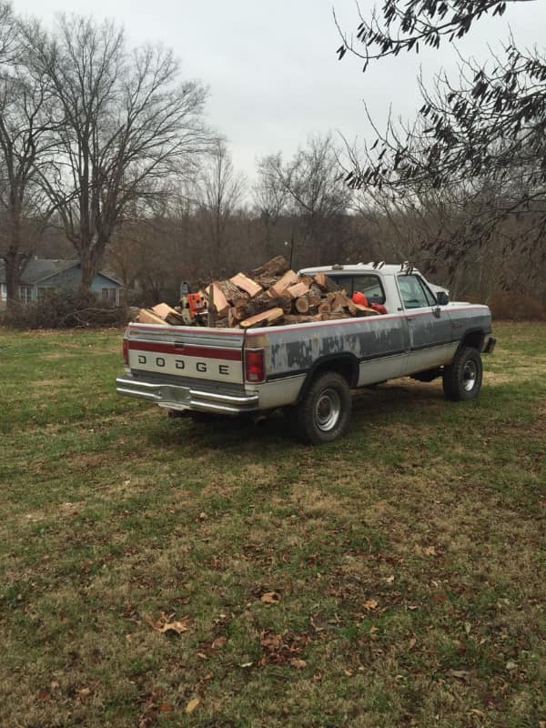 rustic wholesome image of a weathered Dodge pickup truck parked in a field, its bed overflowing with freshly split firewood, symbolizing the quiet satisfaction of a hard day's work in the country.
