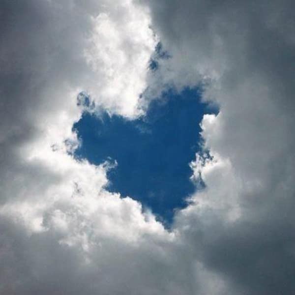 rare and wholesome image of natural wonder where dark storm clouds have split apart to reveal a bright blue sky in the shape of a heart.