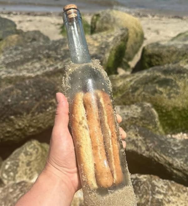 A "cursed" but wholesome meme featuring a glass bottle found on a beach that contains a perfectly preserved hot dog instead of a message, making for a bizarrely funny discovery.