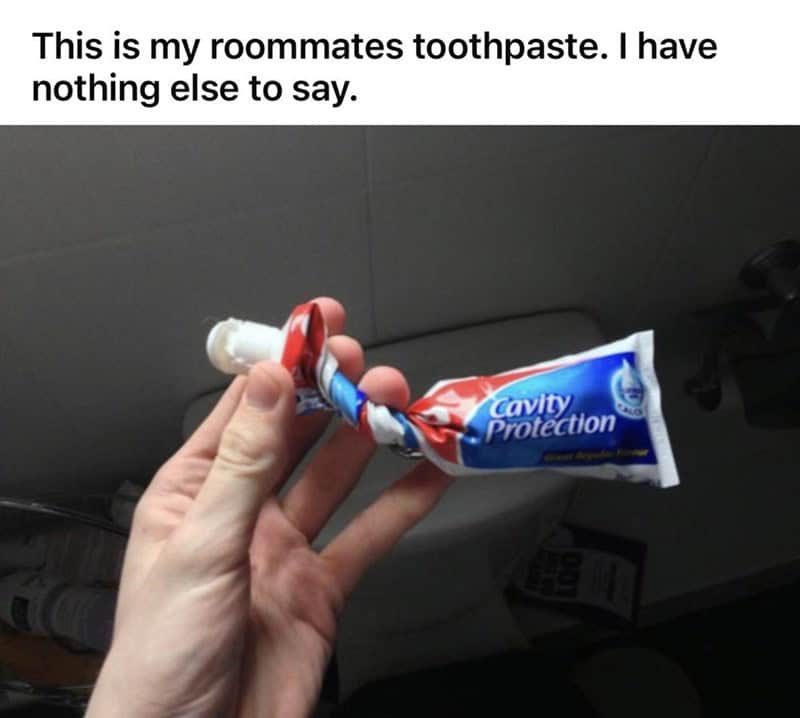 A baffling worst roommates hygiene visual. A hand holds a tube of "Cavity Protection" toothpaste that has been twisted, knotted, and mangled into a gnarled, crumpled mess that looks absolutely impossible to squeeze.