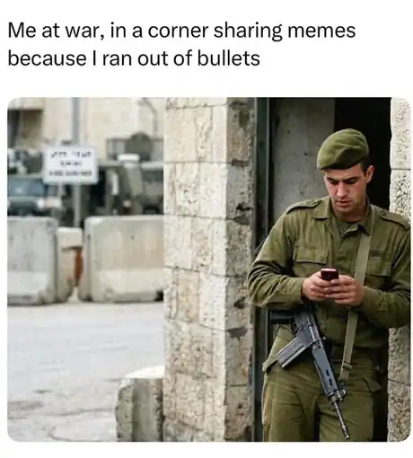 A soldier in a green uniform leaning against a wall checking his phone during war.