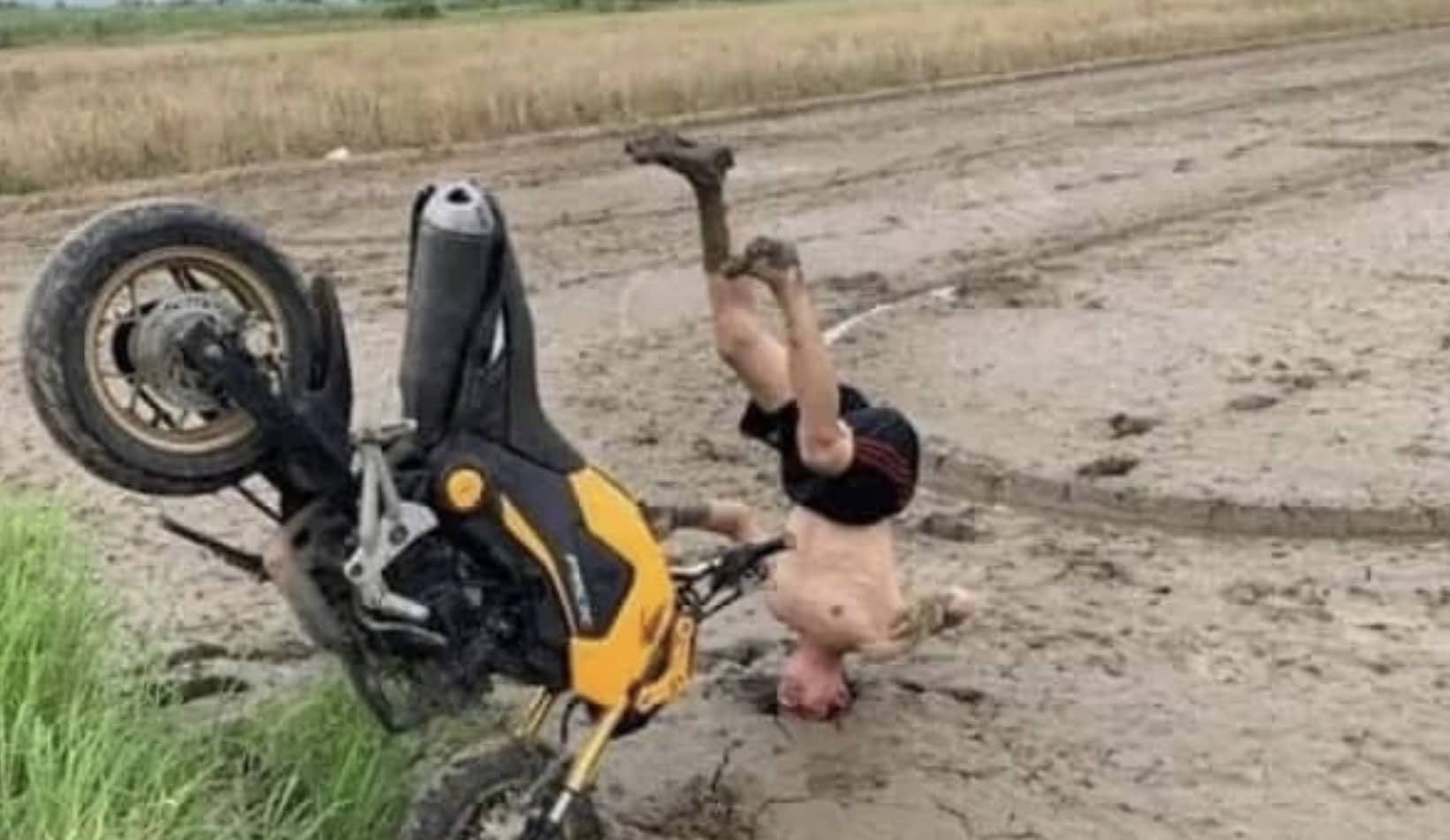A yellow and black motorcycle stuck upright in mud with a rider's head buried in the ground.