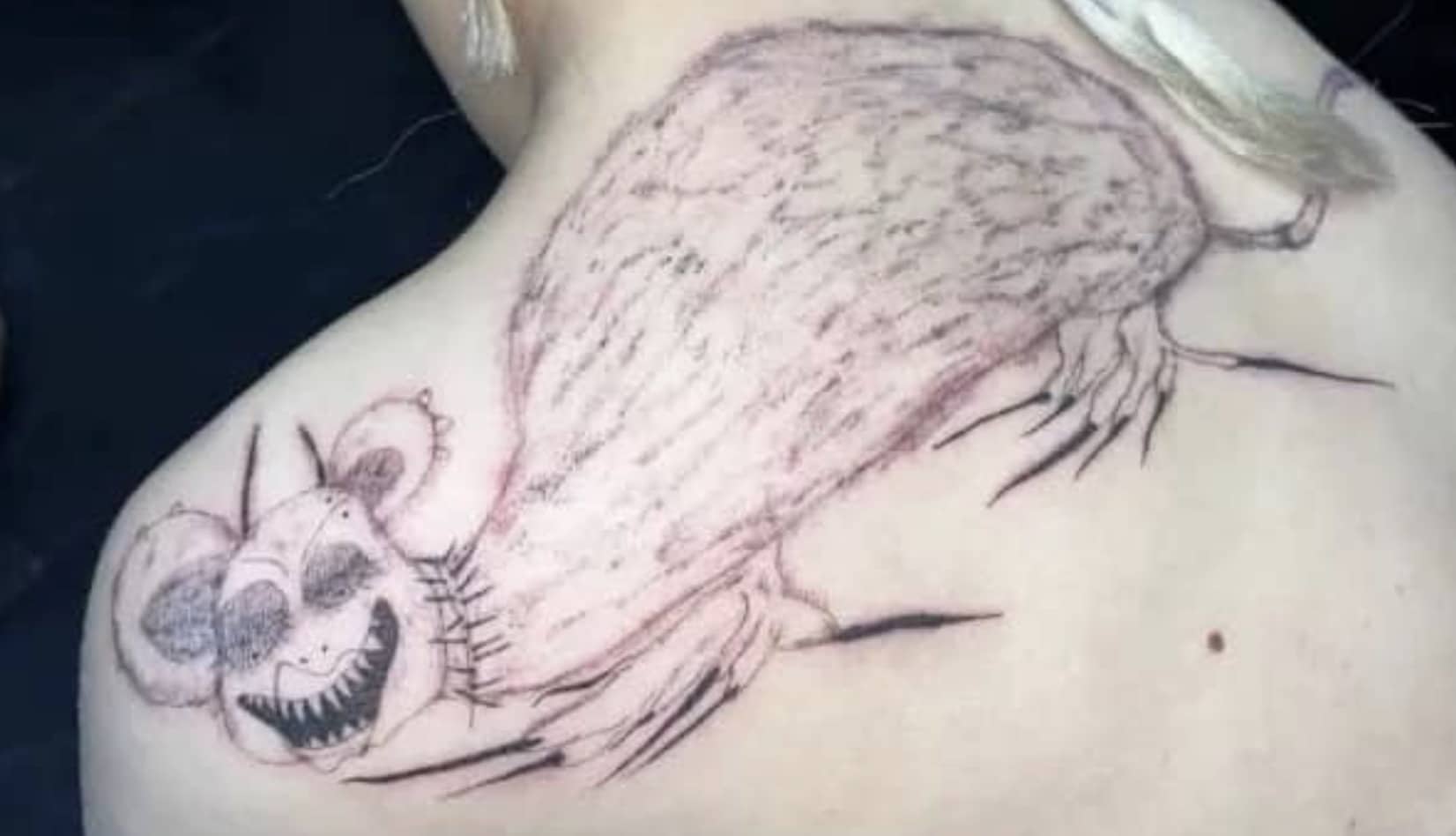 Large poorly executed black ink tattoo on a back featuring a creepy demonic mouse character.