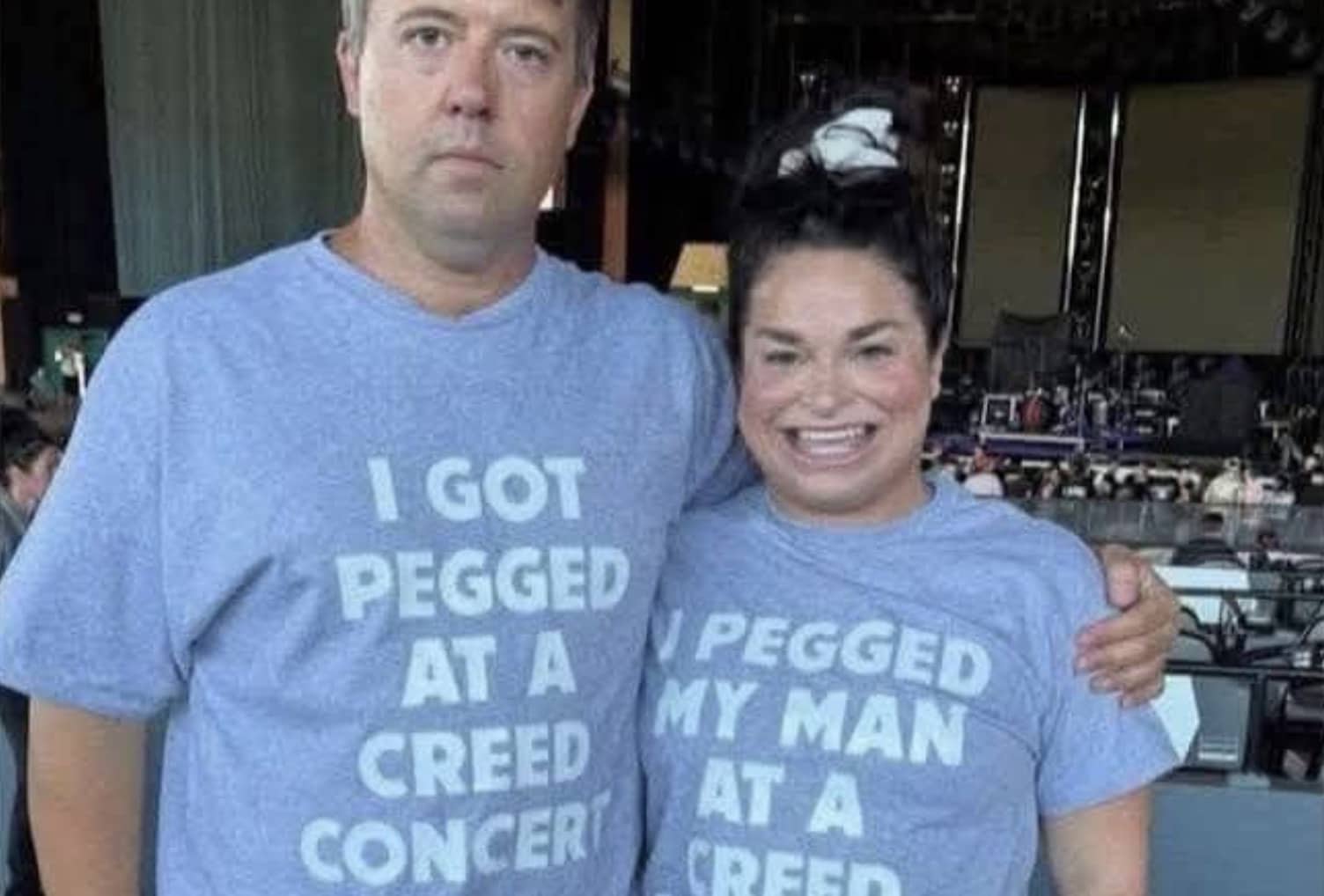 Couple wearing matching blue t-shirts about a specific sexual act at a Creed rock concert.