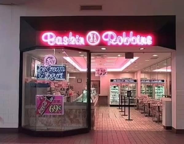 A peak 90s mall glamour shots view of a Baskin-Robbins storefront. The entrance is a neon pink dream, featuring the classic "31" logo and a vintage window poster offering a 32 oz Coca-Cola for just 69 cents.