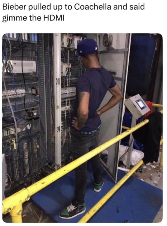 A Bieberchella meme featuring a man in a blue t-shirt and baseball cap standing with his hands on his hips, staring at a massive, chaotic rack of industrial server cables. The caption reads: "Bieber pulled up to Coachella and said gimme the HDMI."
