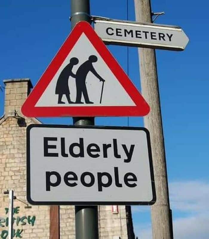 Street sign accidentally pairing an elderly people crossing warning with directional arrow pointing to cemetery.