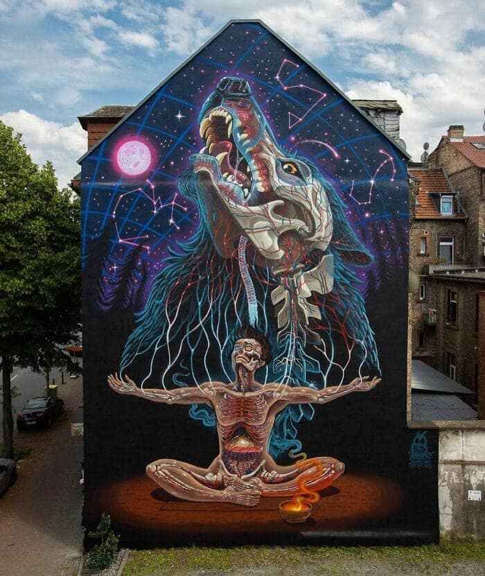 A cosmic, anatomical mural on a tall gable. At the base, a person sits in a meditative pose with their internal organs and skeleton glowing like neon circuits. Emerging from their head is a massive, spectral wolf howling at a pink moon, its own anatomy revealed through translucent fur and celestial constellations.