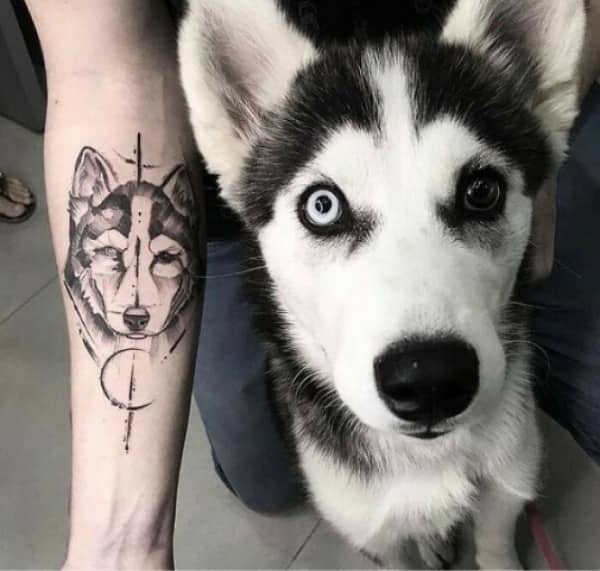 Fine line black and grey tattoo of a husky's face next to a real husky dog.
