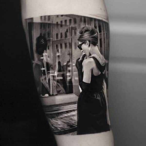 Elegant black and grey tattoo of Audrey Hepburn in Breakfast at Tiffany's looking into a shop window.