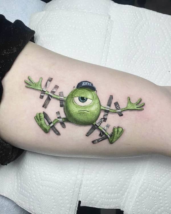 Small colorful tattoo of Mike Wazowski from Monsters Inc taped to an arm with realistic duct tape.