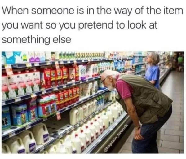 A quiet awkward meme showing an elderly man in a grocery store leaning over to intensely inspect a row of milk jugs. The text explains he’s just killing time: "When someone is in the way of the item you want so you pretend to look at something else."