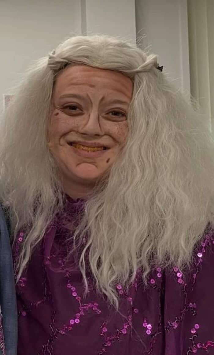 erformer in white wig and purple sequin costume wearing exaggerated old-age wrinkle stage makeup with gold teeth