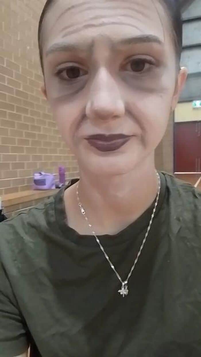 Performer with bald cap and heavy grey contouring stage makeup creating sunken cheeks and aged appearance