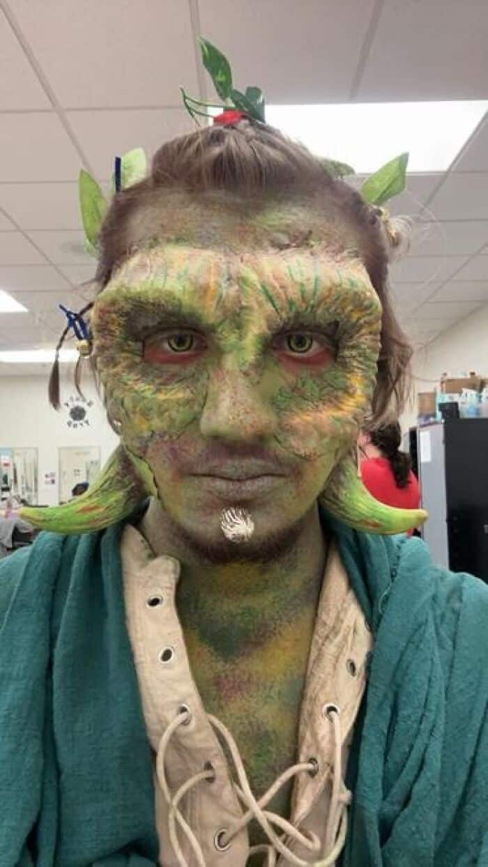 ctor in dramatic green creature stage makeup with horns, leaf accessories, and textured reptilian skin effect