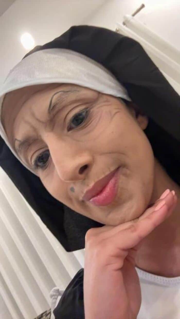 Young performer in nun costume wearing exaggerated elderly stage makeup with drawn-on wrinkles and aged contouring