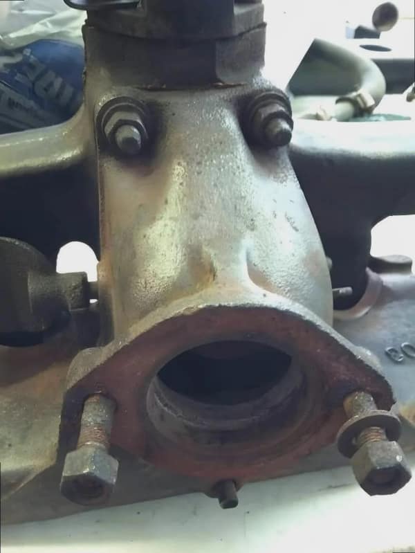 A heavy-duty blursed image showcasing intense pareidolia in a piece of rusted, cast-iron machinery. The arrangement of bolts and the large circular exhaust opening create the perfect silhouette of a face with wide eyes and a mouth frozen in a perpetual, silent scream.