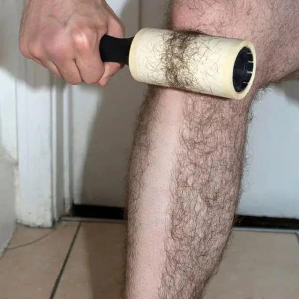 A visceral blursed image showing a person’s extremely hairy leg being "groomed" with a standard adhesive lint roller. The roller has successfully ripped a perfect, thick path of hair from the skin, leaving a smooth trail amidst the forest of leg hair.