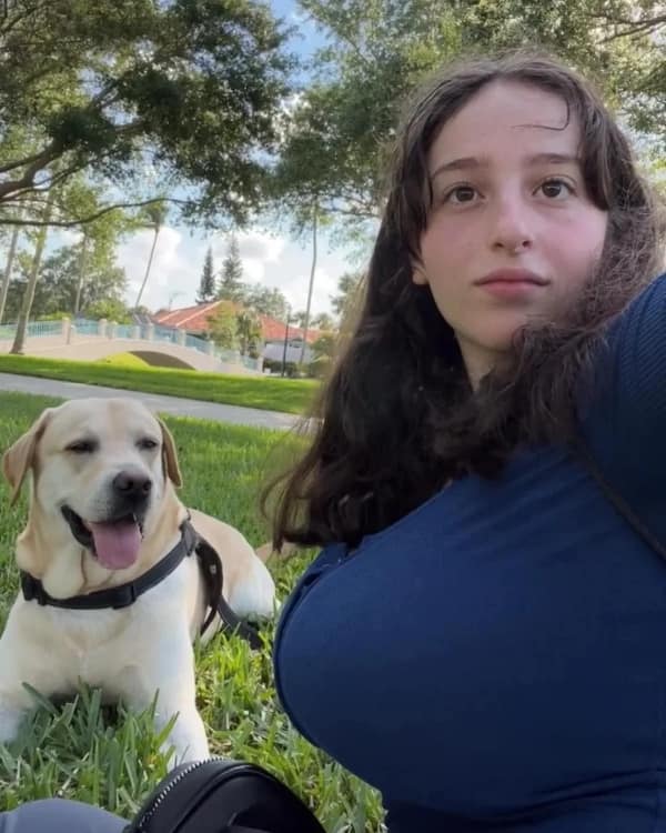 A mind-bending blursed image of a girl taking a selfie with a Labrador. Due to a chaotic optical illusion involving her arm positioning and the dog's back, it creates a jarring and unintended visual that stops the scroll instantly.
