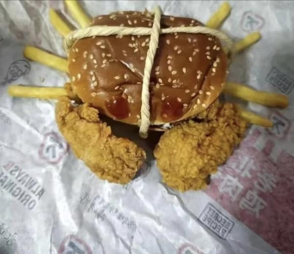 culinary blursed image where a KFC meal has been reassembled into a deep-sea monster. A sesame seed bun acts as the shell, french fries serve as the spindly legs, and two large fried chicken tenders form the massive claws of a "Fast Food Crab."