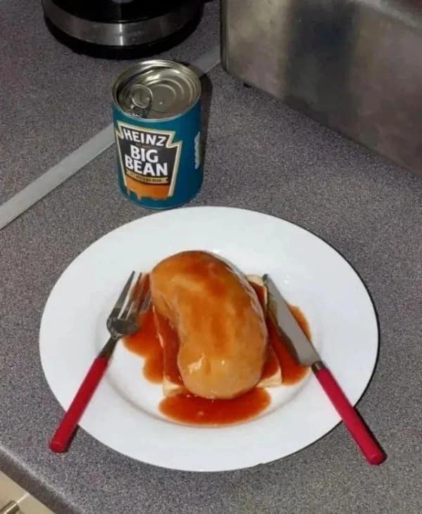 A chaotic blursed image of a meal consisting of a single, massive, kidney-sized baked bean resting on a lone piece of white bread. Behind the plate stands a can of "Heinz BIG BEAN," suggesting a terrifying culinary experiment gone right.