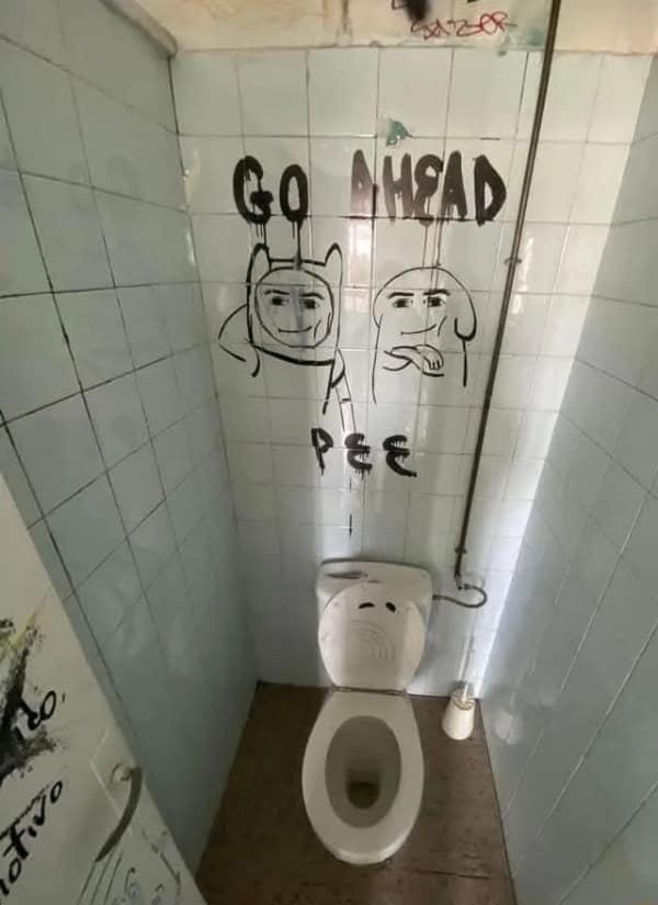 A disturbing blursed image from inside a grimy public toilet. The tiles are covered in graffiti depicting Finn and Jake from Adventure Time but with the smug, realistic "Man Face" from Roblox, staring down at the user with the words "GO AHEAD PEE."