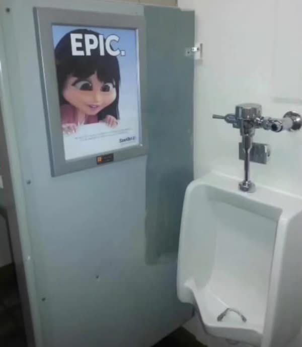 An uncomfortable blursed image from a public restroom. A urinal is mounted next to a divider featuring a large ad with a wide-eyed, animated character who appears to be staring directly at the "target area" of anyone using the facility. The ad is topped with the word "EPIC."