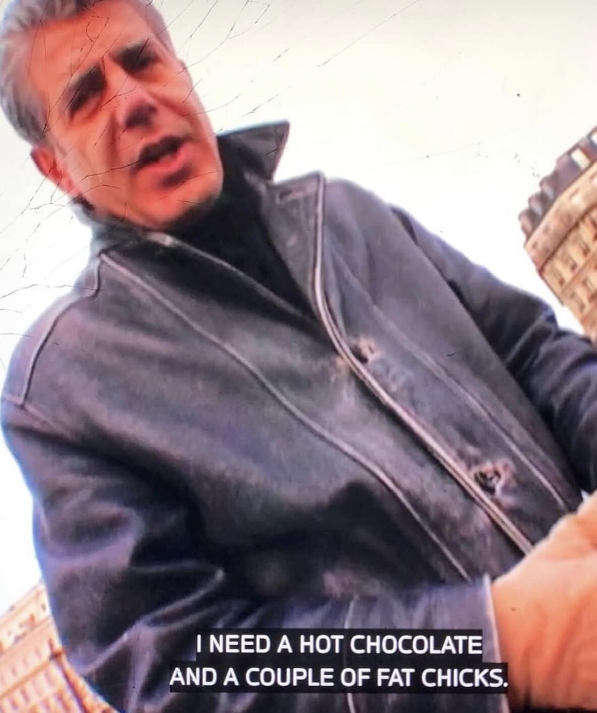 A grainy classic meme captured from a TV screen showing the late Anthony Bourdain. The subtitle at the bottom features a blunt, chaotic request: "I NEED A HOT CHOCOLATE AND A COUPLE OF FAT CHICKS."