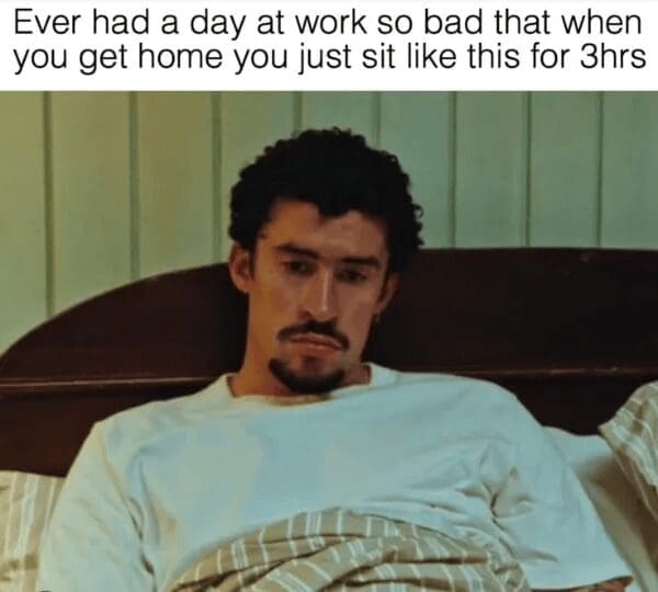 A relatable classic meme featuring artist Bad Bunny sitting on a bed, staring blankly ahead with a soul-crushed expression. The text describes that specific level of workday burnout where you get home and simply sit motionless for three hours.