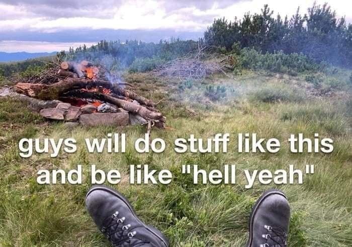 A peak "guy humor" classic meme showing a first-person view of a pair of hiking boots resting in front of a modest bonfire on a grassy hillside. The text perfectly captures the simplicity of male satisfaction: "guys will do stuff like this and be like 'hell yeah'."