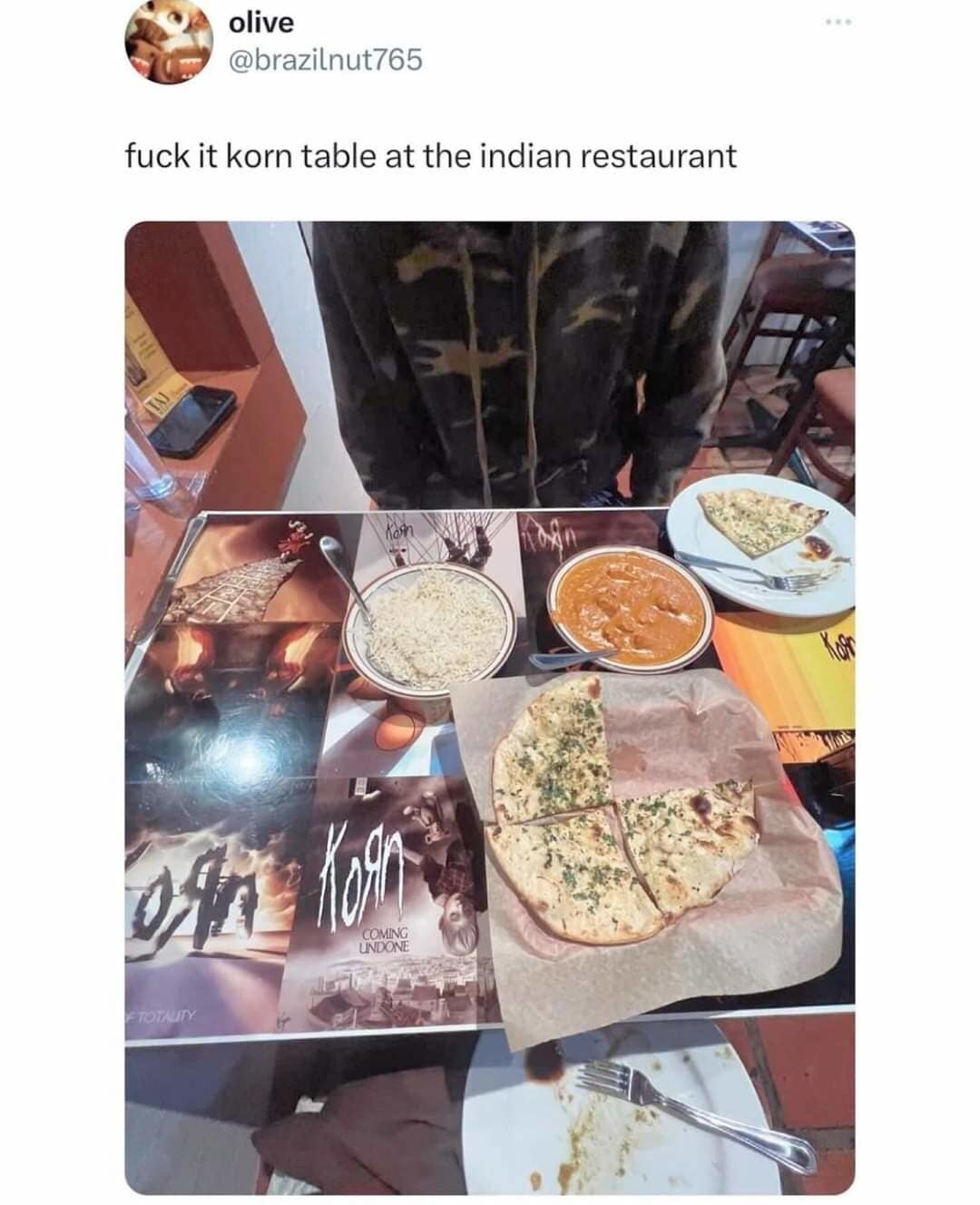 An absurdly specific classic meme featuring a photo of an Indian restaurant table where the placemats are, for some inexplicable reason, a collage of Korn album covers. The caption simply reads: "fuck it korn table at the indian restaurant."