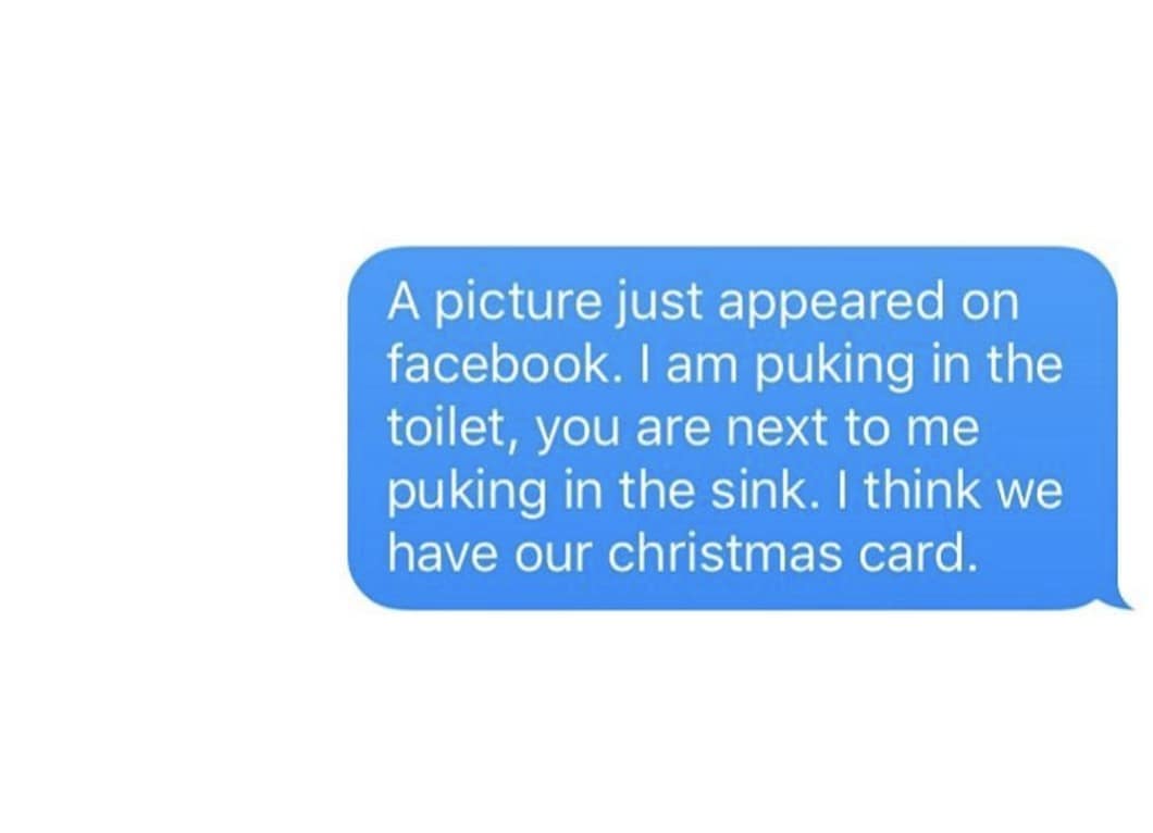 A single blue text message bubble on a white background containing a hilarious prompt often shared as a classic meme for chaotic friendships. The message suggests using a candid photo of two friends simultaneously vomiting as their official holiday greeting card to share with family on Facebook.
