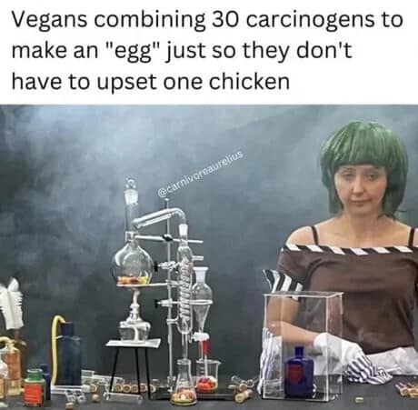 A satirical classic meme featuring a woman in a green wig surrounded by complex laboratory glassware. The text mocks extreme dietary trends, claiming vegans will combine "30 carcinogens" just to synthesize an "egg" without upsetting a single chicken.