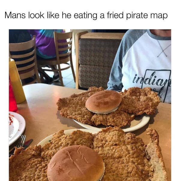 A classic meme taken at a diner, showing a plate with a massive, irregularly shaped breaded pork tenderloin that is roughly four times the size of the tiny hamburger bun resting on top of it. The text jokes: "Mans look like he eating a fried pirate map".