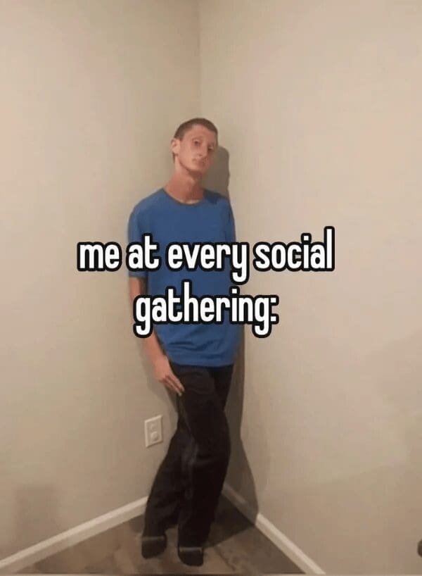A peak social anxiety classic meme featuring a man leaning stiffly and uncomfortably into the corner of a room, seemingly trying to disappear into the drywall. The text reads: "me at every social gathering."