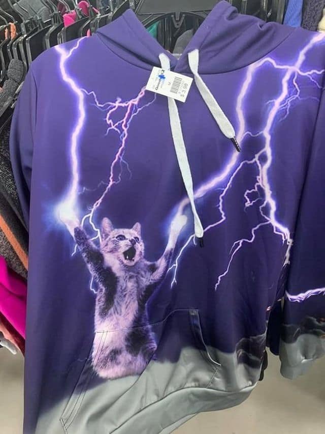 A majestic classic meme found in the wild. This photo captures a purple thrift-store hoodie featuring an airbrushed graphic of a domestic cat shooting massive bolts of lightning from its outstretched paws, looking like a feline version of Emperor Palpatine.