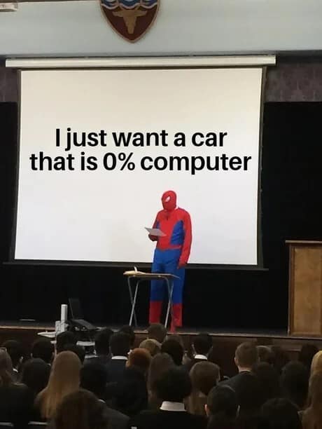 A person in a Spider-Man suit gives a presentation in front of an assembly, a setup often seen in a classic meme rotation. The slide behind him declares a simple, heartfelt desire for a modern car that contains zero percent computer components.