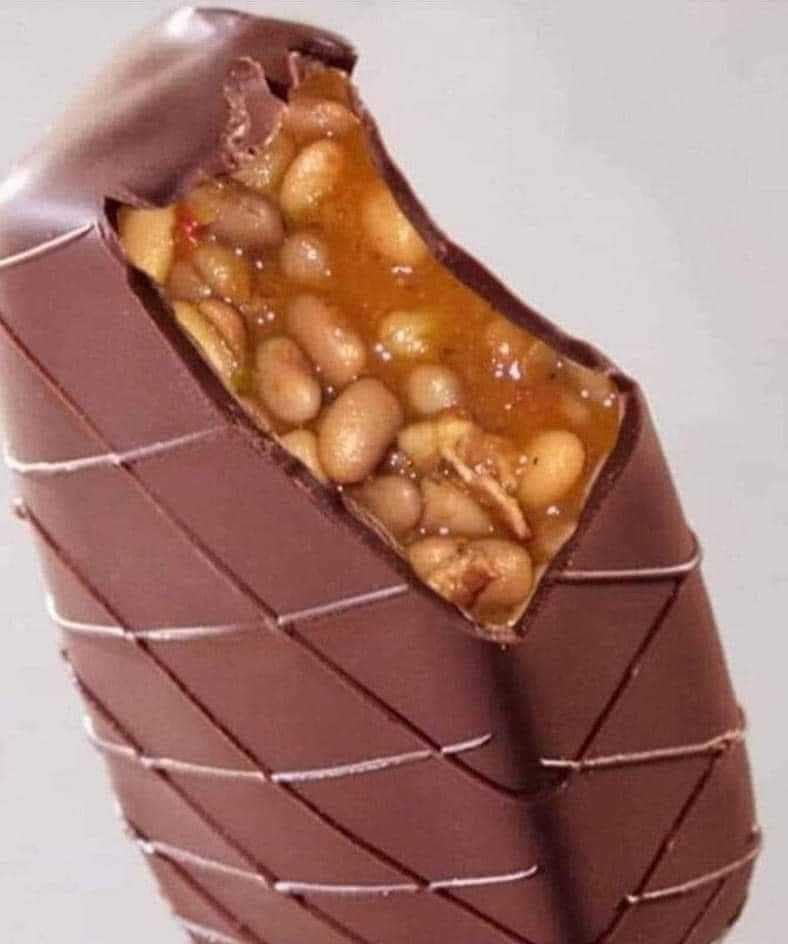 A "cursed" classic meme featuring a high-resolution photo of a chocolate bar that has been bitten into. Instead of a typical nougat or caramel filling, the inside is revoltingly stuffed with saucy baked beans, subverting every expectation of a sweet treat.
