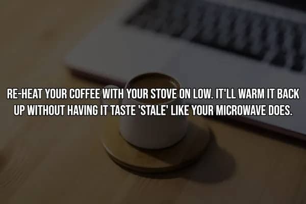 White mug on wooden coaster beside laptop keyboard, demonstrating proper stovetop coffee reheating method.