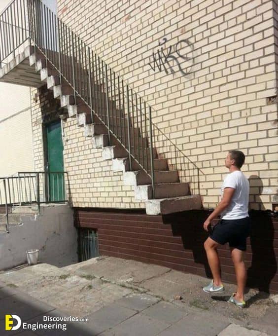 Man stares up at outdoor staircase with no ground-level access built against brick building wall