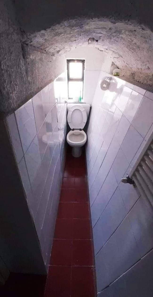 Extremely narrow tunnel-like bathroom with toilet wedged at the far end barely accessible by adults