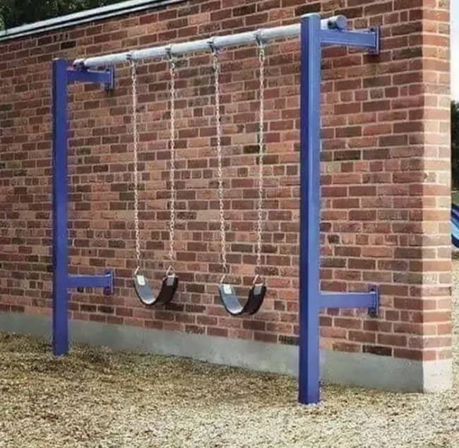 Playground swings installed flush against brick wall leaving zero clearance for children to swing safely
